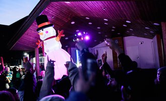 © Kleinwalsertal Tourismus | Oliver Farys A festive event with a large snowman puppet and many celebrating people. Colorful lights illuminate the scene. | © Kleinwalsertal Tourismus | Oliver Farys