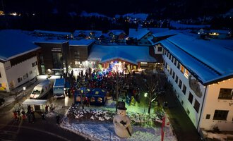 © Kleinwalsertal Tourismus eGen | Oliver Farys A festive event in a snowy village at night. People are gathered around a stage while a large snowman stands nearby. | © Kleinwalsertal Tourismus eGen | Oliver Farys