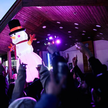© Kleinwalsertal Tourismus | Oliver Farys A festive event with a large snowman puppet and many celebrating people. Colorful lights illuminate the scene. | © Kleinwalsertal Tourismus | Oliver Farys
