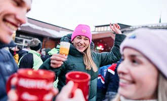 © Kleinwalsertal Tourismus | Oliver Farys A cheerful group of people in winter clothing is celebrating outdoors. A woman with a pink hat is holding a drink and smiling. | © Kleinwalsertal Tourismus | Oliver Farys