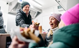 © Kleinwalsertal Tourismus | Oliver Farys A vendor serves ice cream to happy customers in a food truck. The two women are laughing and enjoying the delicious treats. | © Kleinwalsertal Tourismus | Oliver Farys