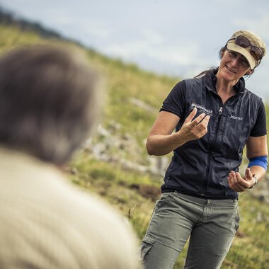 A woman is talking to a man outdoors. She is holding an object in her hand and smiling kindly. | © Kleinwalsertal Tourismus | Oliver Farys