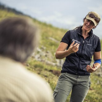 © Kleinwalsertal Tourismus | Oliver Farys A woman is talking to a man outdoors. She is holding an object in her hand and smiling kindly. | © Kleinwalsertal Tourismus | Oliver Farys