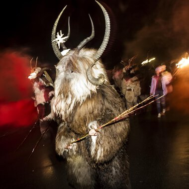 © Kleinwalsertal Tourismus | Dominik Berchtold A festive parade with masked participants in animal costumes. The dark background is illuminated by red flares. | © Kleinwalsertal Tourismus | Dominik Berchtold