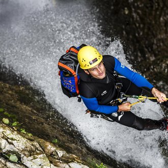 © Bergschule Kleinwalsertal | Dominik Berchtold A man is climbing a steep rock wall in a waterfall. He is wearing a helmet and climbing gear. | © Bergschule Kleinwalsertal | Dominik Berchtold