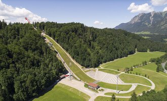 © Skiflugschanze Oberstdorf | Eren Karaman An impressive ski jump surrounded by green forests and mountains. The landscape is picturesque and showcases a mix of nature and sports facilities. | © Skiflugschanze Oberstdorf | Eren Karaman