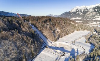 © Skiflugschanze Oberstdorf | Eren Karaman A snow-covered landscape with trees and a clear sky. In the background, mountains can be seen that complement the wintry scenery. | © Skiflugschanze Oberstdorf | Eren Karaman