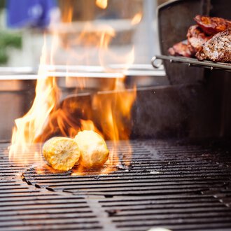© Hotel Auenhütte | Eva Backes A grill with flames on which food is cooked. Grilled potatoes and meat can be seen. | © Hotel Auenhütte | Eva Backes
