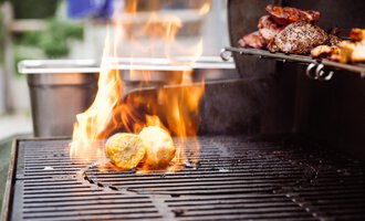 A grill with flames on which food is cooked. Grilled potatoes and meat can be seen. | © Hotel Auenhütte | Eva Backes