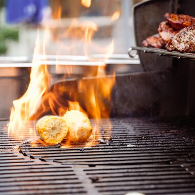 A grill with flames on which food is cooked. Grilled potatoes and meat can be seen. | © Hotel Auenhütte | Eva Backes