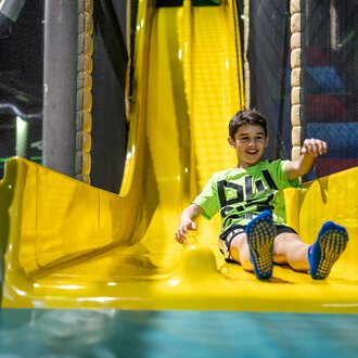 A cheerful boy slides down a yellow slide in a playground. The space is designed to be colorful and inviting. | © Wonnemar Sonthofen | interSPA Gruppe