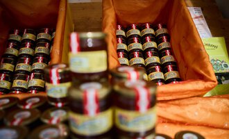 A variety of small jars of jam are placed in orange baskets. The jars are arranged in rows and have colored labels. | © Kleinwalsertal Tourismus | Oliver Farys