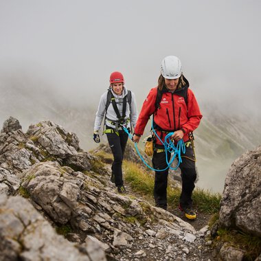 Two mountaineers are moving along a rocky slope. It is foggy, and the surroundings appear wild and untouched. | © Bergschule Kleinwalsertal | Oliver Farys