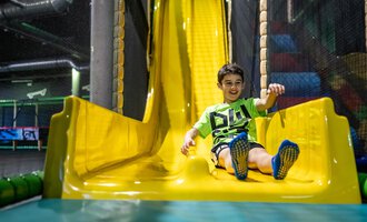 © Wonnemar Sonthofen | interSPA Gruppe A smiling child happily slides down a yellow slide. In the background, playground equipment can be seen. | © Wonnemar Sonthofen | interSPA Gruppe