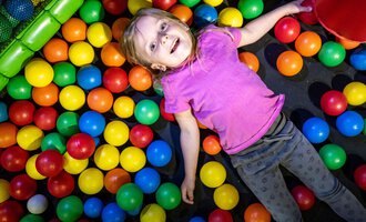 © Wonnemar Sonthofen | interSPA Gruppe A happy child is lying in a ball pit filled with colorful balls. She is wearing a purple T-shirt and looks relaxed. | © Wonnemar Sonthofen | interSPA Gruppe
