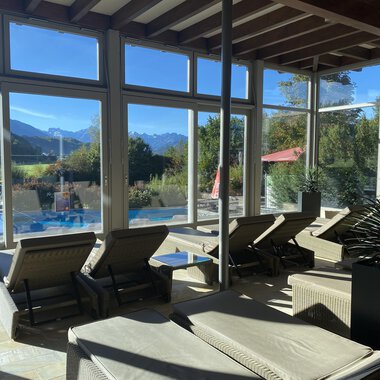 © Wonnemar Sonthofen | interSPA Gruppe A bright relaxation room with loungers and large windows. In the background, mountains and a pool are visible. | © Wonnemar Sonthofen | interSPA Gruppe