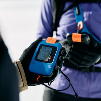 © Kleinwalsertal Tourismus | Oliver Farys A person is holding a transceiver device in their hand. In the background, a snowy area is visible. | © Kleinwalsertal Tourismus | Oliver Farys