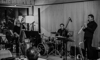 © Naturhotel Chesa Valisa Three musicians are happily gathered together, playing various instruments. In the background, the nature hotel can be seen. | © Naturhotel Chesa Valisa