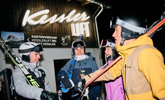 © Kleinwalsertal Tourismus | Oliver Farys A pair of skiers is preparing for night skiing. In the background, other skiers and a lit ski lift can be seen. | © Kleinwalsertal Tourismus | Oliver Farys