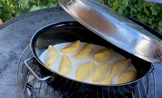 A pot filled with dumplings is opened on a grill. In the background, green plants and flowers can be seen. | © Gerd am Herd | Gerd Hammerer