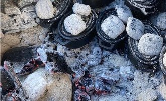 Several small pots are lying in ash and charcoal embers. The scene conveys an impression of cooking over an open fire. | © Gerd am Herd | Gerd Hammerer