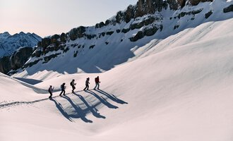 © Kleinwalsertal Tourismus eGen | Oliver Farys A group of hikers is walking through a snowy landscape. Majestic mountains can be seen in the background. | © Kleinwalsertal Tourismus eGen | Oliver Farys