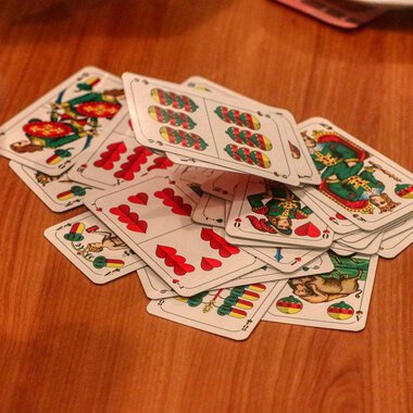 A stack of cards lies on a wooden table. A hand is visible, encircling the cards. | © Chesa Valisa