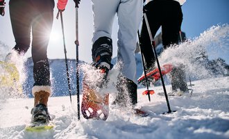 © Kleinwalsertal Tourismus | Oliver Farys Three people are hiking in the snow with snowshoes. The sun is shining and snow is spraying from their movements. | © Kleinwalsertal Tourismus | Oliver Farys