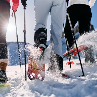 © Kleinwalsertal Tourismus | Oliver Farys Three people are hiking in the snow with snowshoes. The sun is shining and snow is spraying from their movements. | © Kleinwalsertal Tourismus | Oliver Farys
