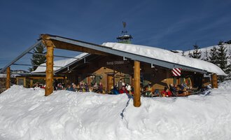 © Bergstüble | Michaela Beck Dornach Eine gemütliche Berghütte im Schnee mit Gästen auf der Terrasse. Der Himmel ist klar und blau, und die Umgebung ist winterlich. | © Bergstüble | Michaela Beck Dornach