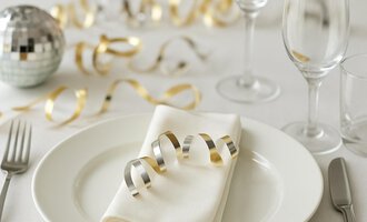 Ein festlich gedeckter Tisch mit einer roten Kerze und einem Weihnachtsstern. Die Dekoration ist von Tannenzweigen und Beeren umgeben. | © KI generiert Kleinwalsertal Tourismus