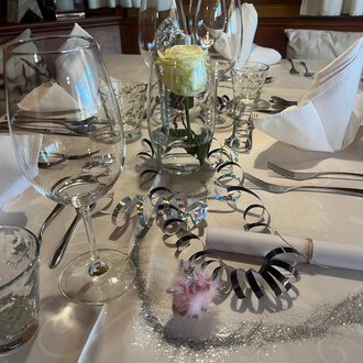 Two champagne glasses toast on a festively decorated table. In the background, red Christmas ornaments and golden decorations can be seen. | © Genuss- & Aktivhotel Sonnenburg
