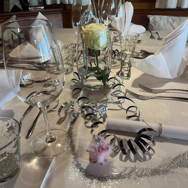 © Genuss- & Aktivhotel Sonnenburg Two champagne glasses toast on a festively decorated table. In the background, red Christmas ornaments and golden decorations can be seen. | © Genuss- & Aktivhotel Sonnenburg
