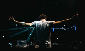 © dj let´s fetz Ein DJ steht mit weit ausgebreiteten Armen hinter seinem Mischpult. Bunte Lichter strahlen im Hintergrund und schaffen eine festliche Stimmung. | © dj let´s fetz