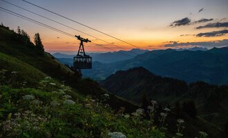 A cable car travels over hilly mountains at sunset. The sky is illuminated in warm colors. | © OBERSTDORF · KLEINWALSERTAL BERGBAHNEN