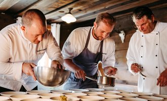 Three chefs are working intently in a rustic kitchen. They are preparing dishes in white bowls and using various cooking utensils. | © Kleinwalsertal Tourismus eGen | Oliver Farys