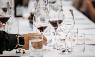 An elegantly set table with wine glasses and water jugs. In the foreground, a hand is seen holding a water glass. | © Kleinwalsertal Tourismus eGen | Oliver Farys