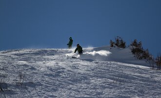 © Markus Hoefler Two skiers are going down a snow-covered slope. The sky is clear and blue. | © Markus Hoefler