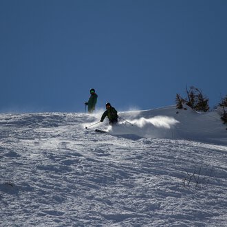 © Markus Hoefler Zwei Skifahrer fahren über einen schneebedeckten Hang. Der Himmel ist klar und blau. | © Markus Hoefler