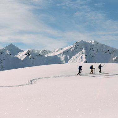 © Kleinwalsertal Tourismus | Oliver Farys A skier in a blue suit is skiing through fresh, powdery snow. In the background, snow-covered mountains and a clear blue sky can be seen. | © Kleinwalsertal Tourismus | Oliver Farys