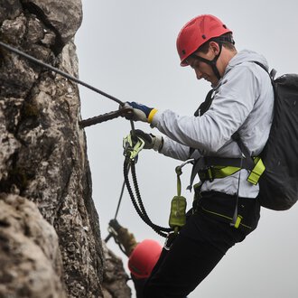 © Bergschule Kleinwalsertal | Oliver Farys A climber is secured to a rock wall and is focusing on his technique. In the background, another climber can be seen, while a misty atmosphere prevails. | © Bergschule Kleinwalsertal | Oliver Farys