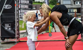A cheerful girl hands a medal to an athlete after a competition. The atmosphere is characterized by joy and pride. | © Kleinwalsertal Tourismus - Dominik Berchtold