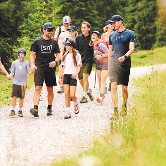 © Kleinwalsertal Tourismus | Oliver Farys A group of people is hiking on a narrow path through nature. Surrounded by green trees, they enjoy the fresh air and each other's company. | © Kleinwalsertal Tourismus | Oliver Farys