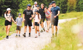 A group of people is hiking on a narrow path through nature. Surrounded by green trees, they enjoy the fresh air and each other's company. | © Kleinwalsertal Tourismus | Oliver Farys