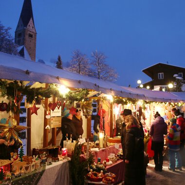 © Kleinwalsertal Tourismus | Frank Drechsel A festive Christmas market with numerous stalls under a tent. It is dark, and the lighting creates an inviting atmosphere. | © Kleinwalsertal Tourismus | Frank Drechsel