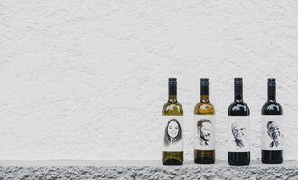 © Das Naturhotel Chesa Valisa Four bottles of wine are placed on a gray surface. The labels display black-and-white portraits of different individuals. | © Das Naturhotel Chesa Valisa