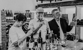 A group of three people is enjoying wine in a wine shop. They are holding glasses in their hands and are looking intently at the glasses. | © Das Naturhotel Chesa Valisa