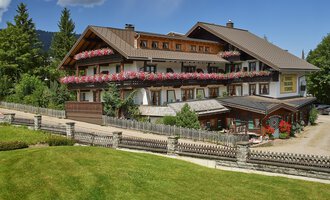 A charming, multi-story building with flowers on the balcony. Surrounded by a well-maintained garden and trees.