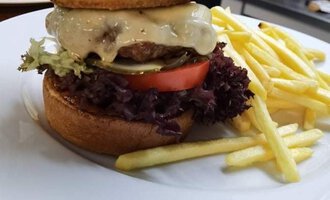 A large burger with two buns, a meat patty, cheese, lettuce, and tomato. French fries are on the plate.