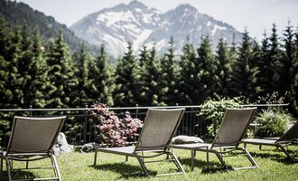 Eine ruhige Terrasse mit Liegestühlen und Blick auf majestätische Berge. Im Hintergrund sind dabei grüne Bäume und bunte Pflanzen zu sehen. | © Verwöhn- & Wellnesshotel Walserhof| Aileen Melucci